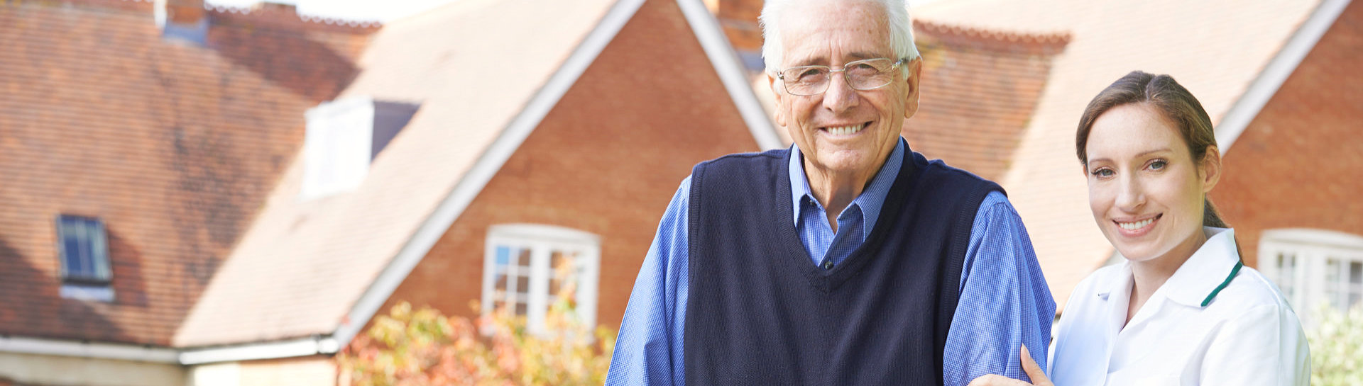 Caregiver helps senior man to walk in garden using walking frame